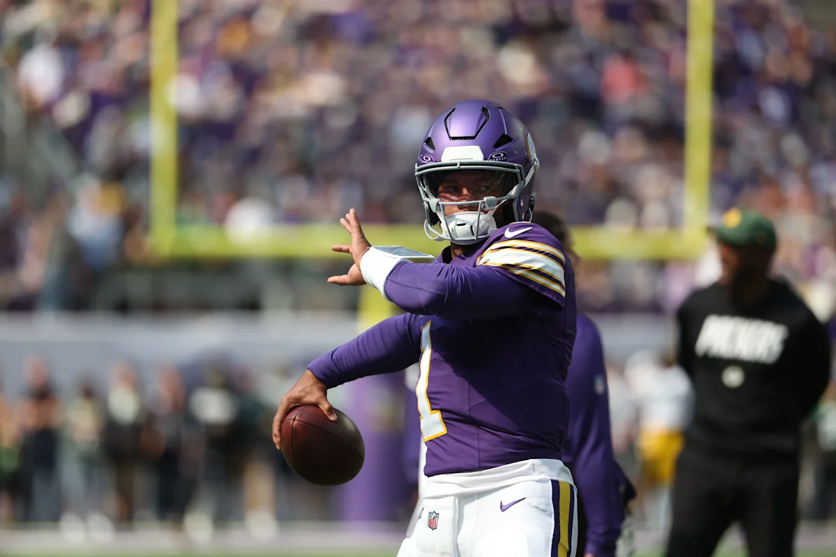Football player in purple uniform throws a football on a sunlit field.