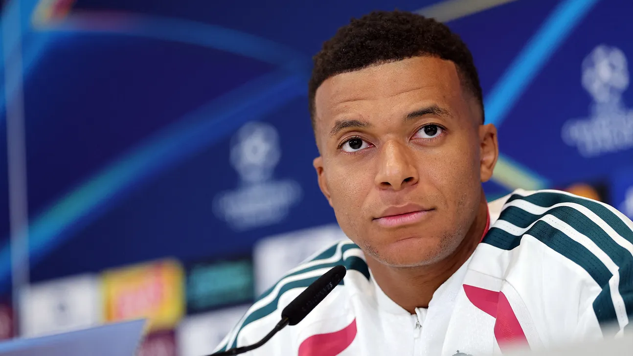 Kylian Mbappé wearing a white sports jacket during a press conference