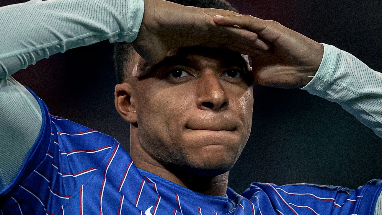 Footballer in a blue striped jersey raises a hand to his forehead during a match.