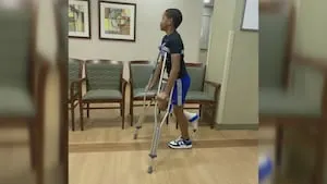 Young person walks through a hallway using forearm crutches while wearing a leg brace.