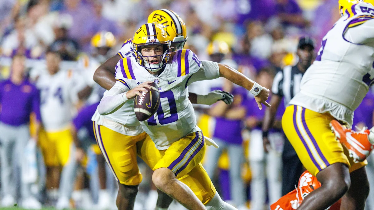 LSU football player runs with the ball as teammates block defenders during a game.