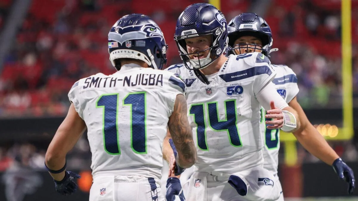 Three Seattle Seahawks players in white uniforms celebrate together on the field during a game.