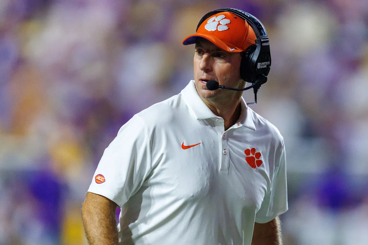 Clemson football coach wearing headset and orange cap on sideline during a game