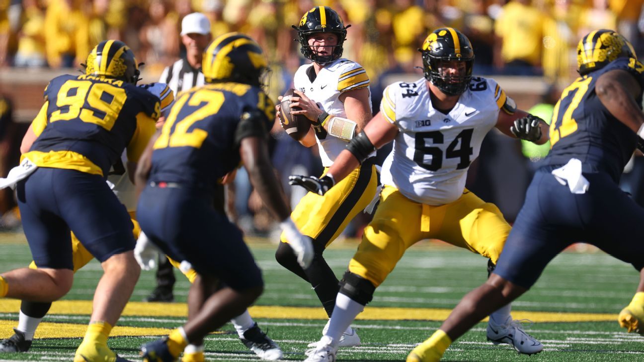 Iowa quarterback holds the football as teammates block Michigan defenders during a game.