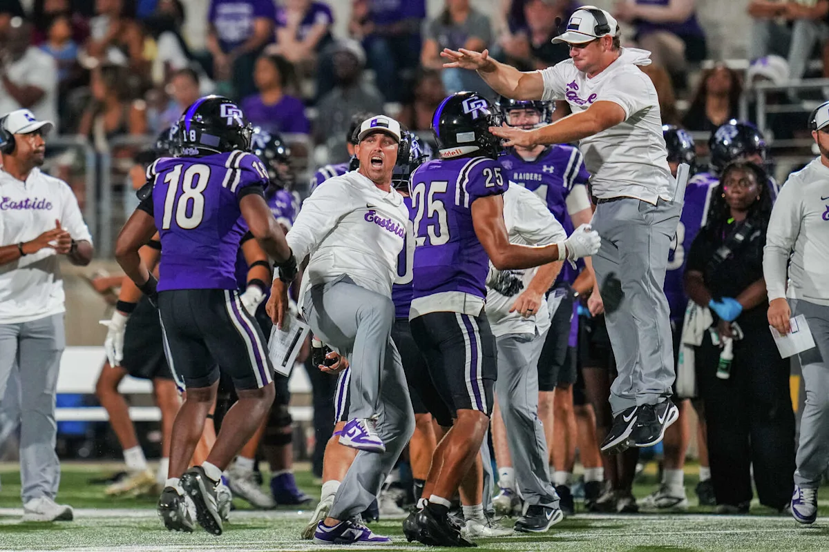Football players and coaches in purple and white celebrate energetically along the sideline.