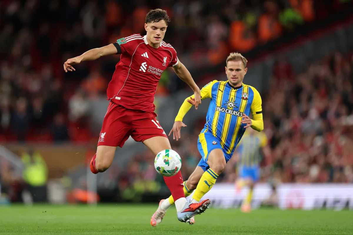 Liverpool player in red controls the ball as an opponent in yellow and blue challenges.