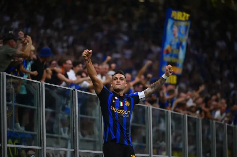 Footballer in blue-and-black jersey raises both fists before cheering supporters
