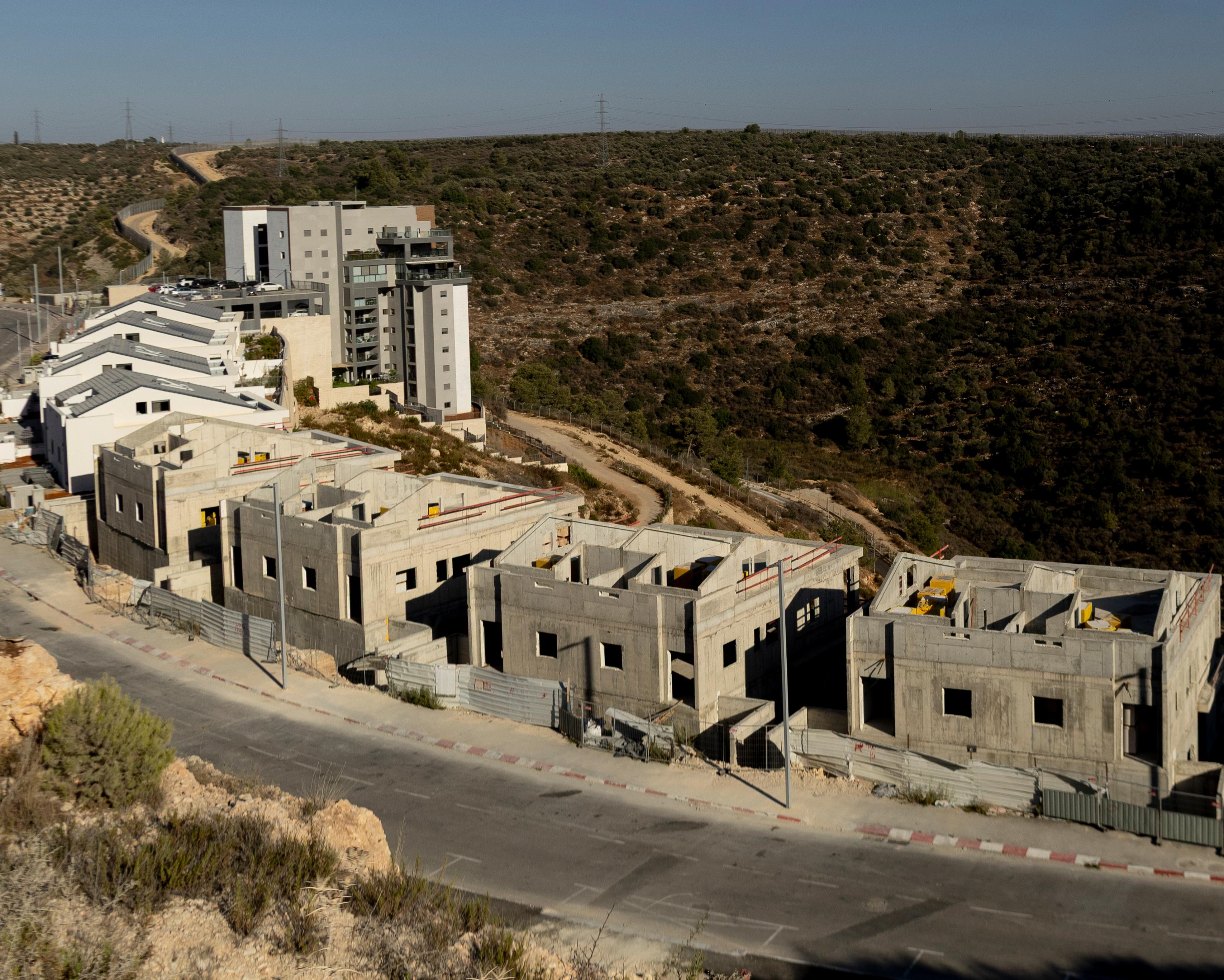 Aerial view of unfinished concrete homes beside completed apartments and scrub-covered terrain