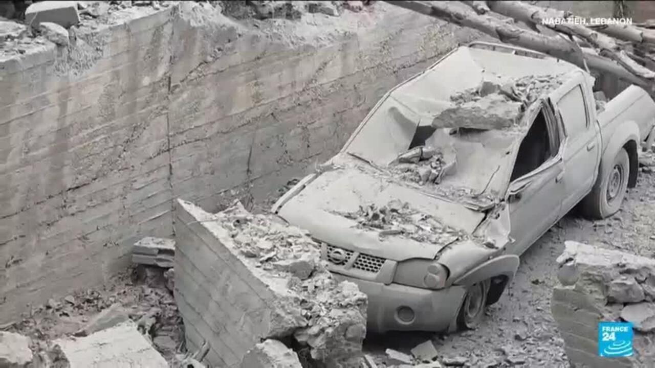 Damaged pickup truck buried beneath rubble beside a collapsed concrete wall.