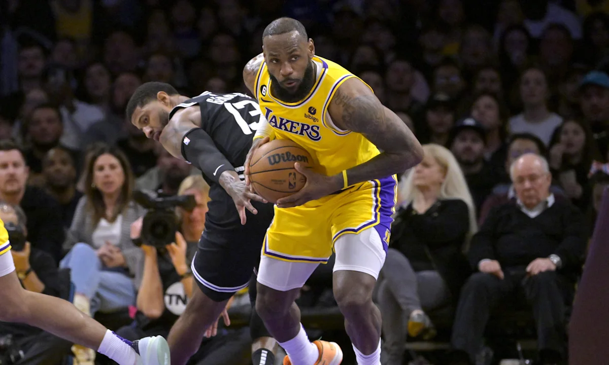 A Lakers player in yellow drives toward the basket while holding the ball against a defender.