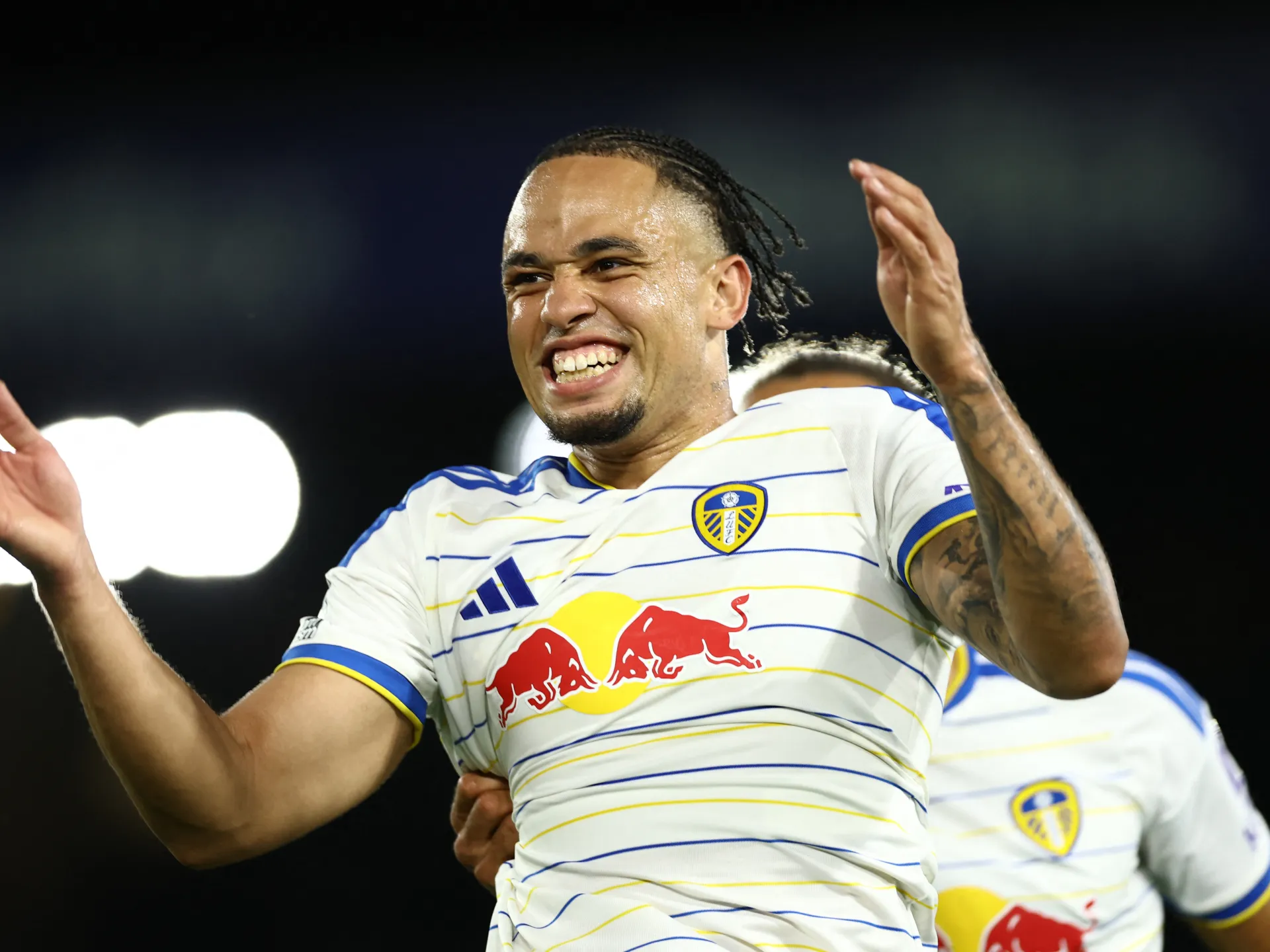 Leeds United player celebrates during a match, raising his hands with a teammate behind him