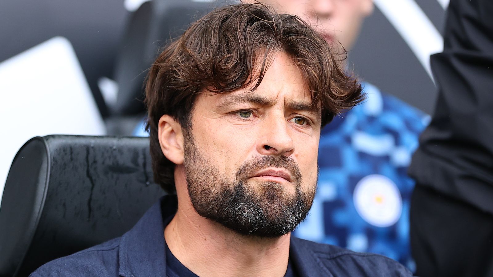 Close-up of a bearded man with tousled brown hair looking serious from a stadium seat