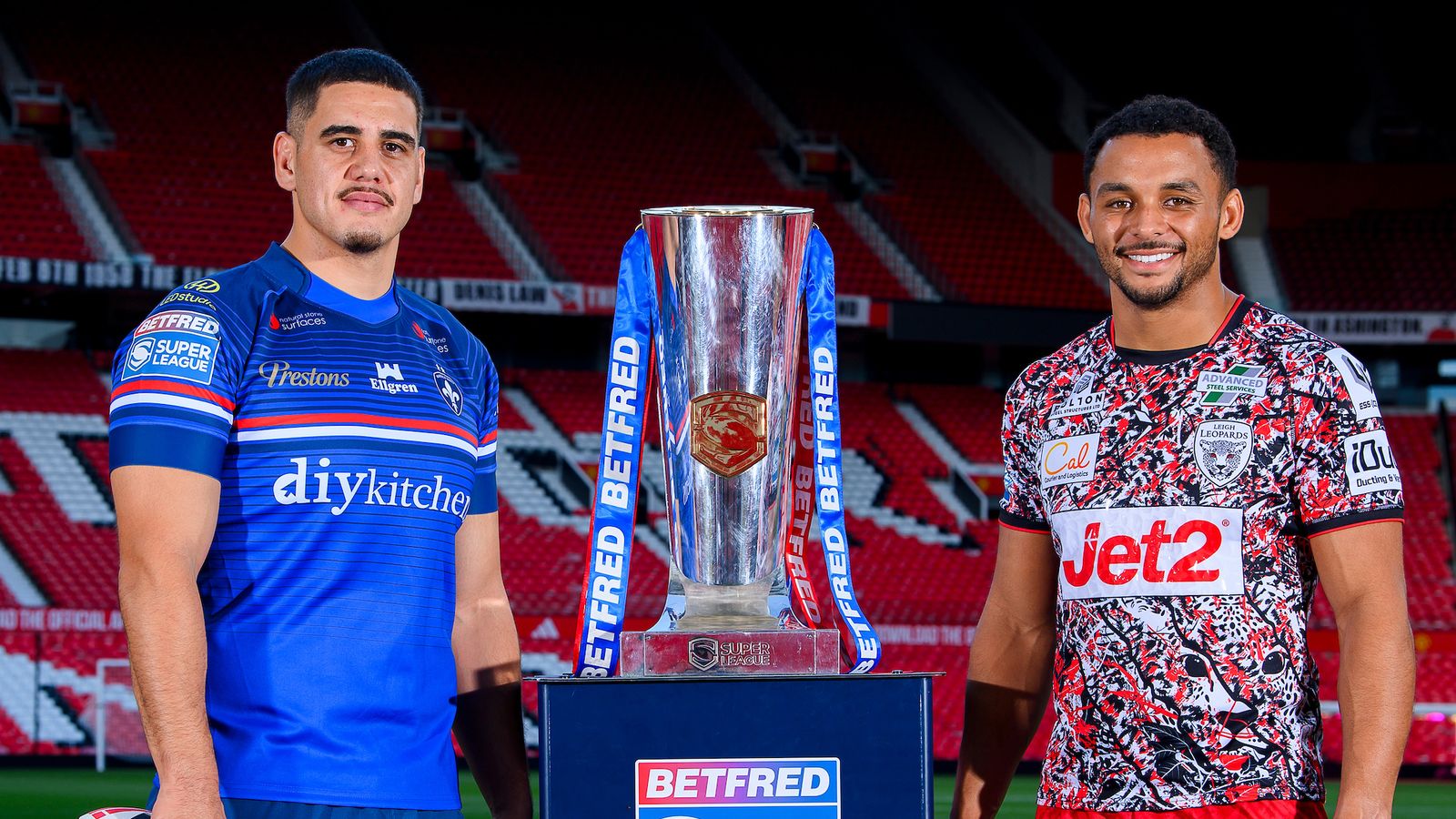 Two rugby players pose beside a silver trophy in a stadium