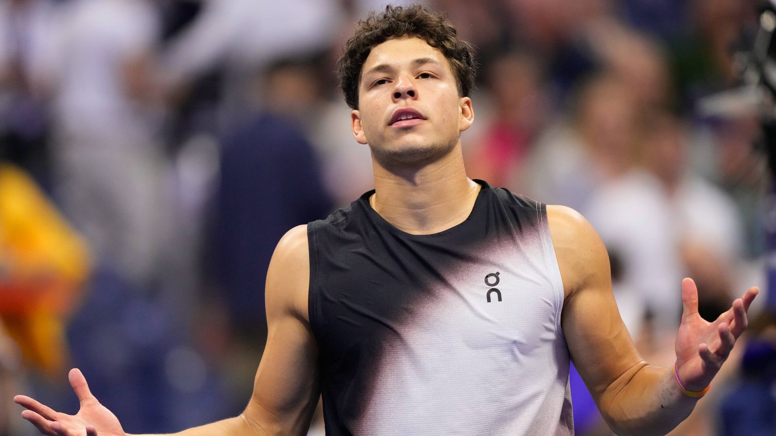 Tennis player in black and gray sleeveless shirt gestures with both hands during a match
