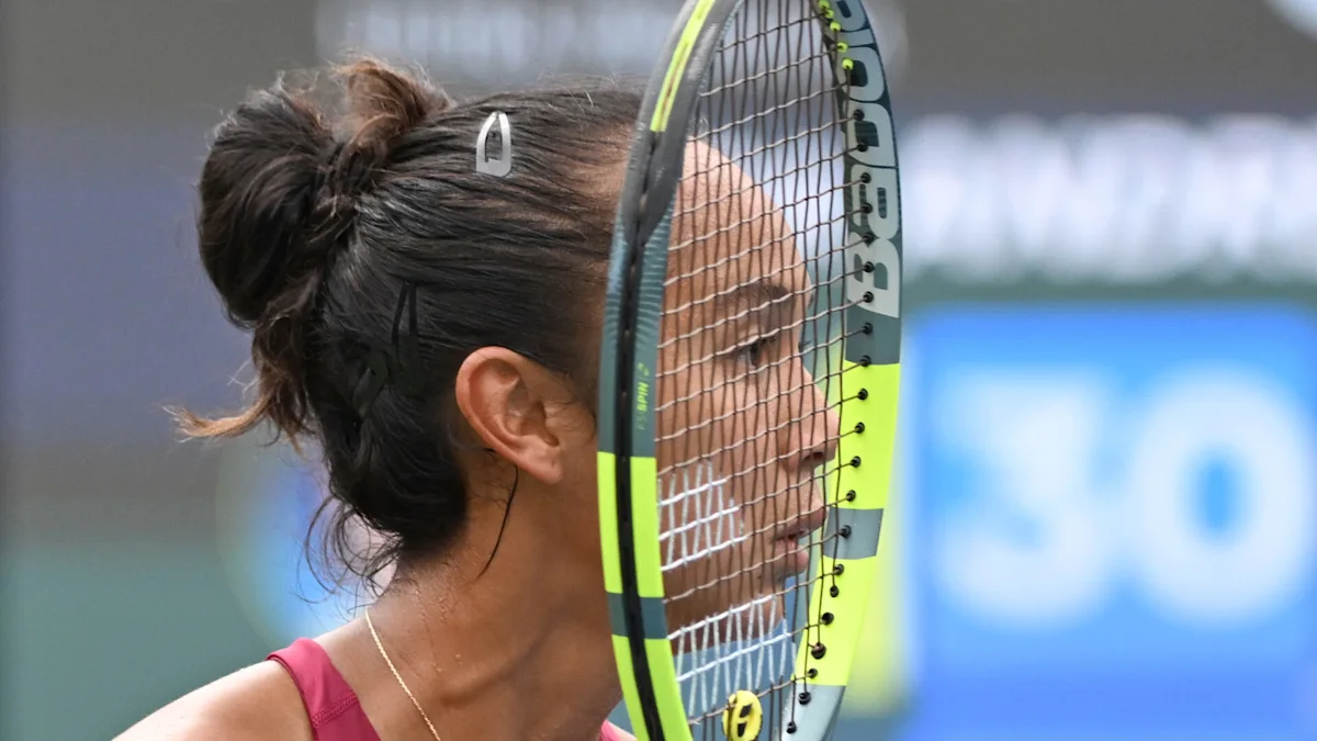 Close-up of a tennis player holding a racket in front of her face on court.