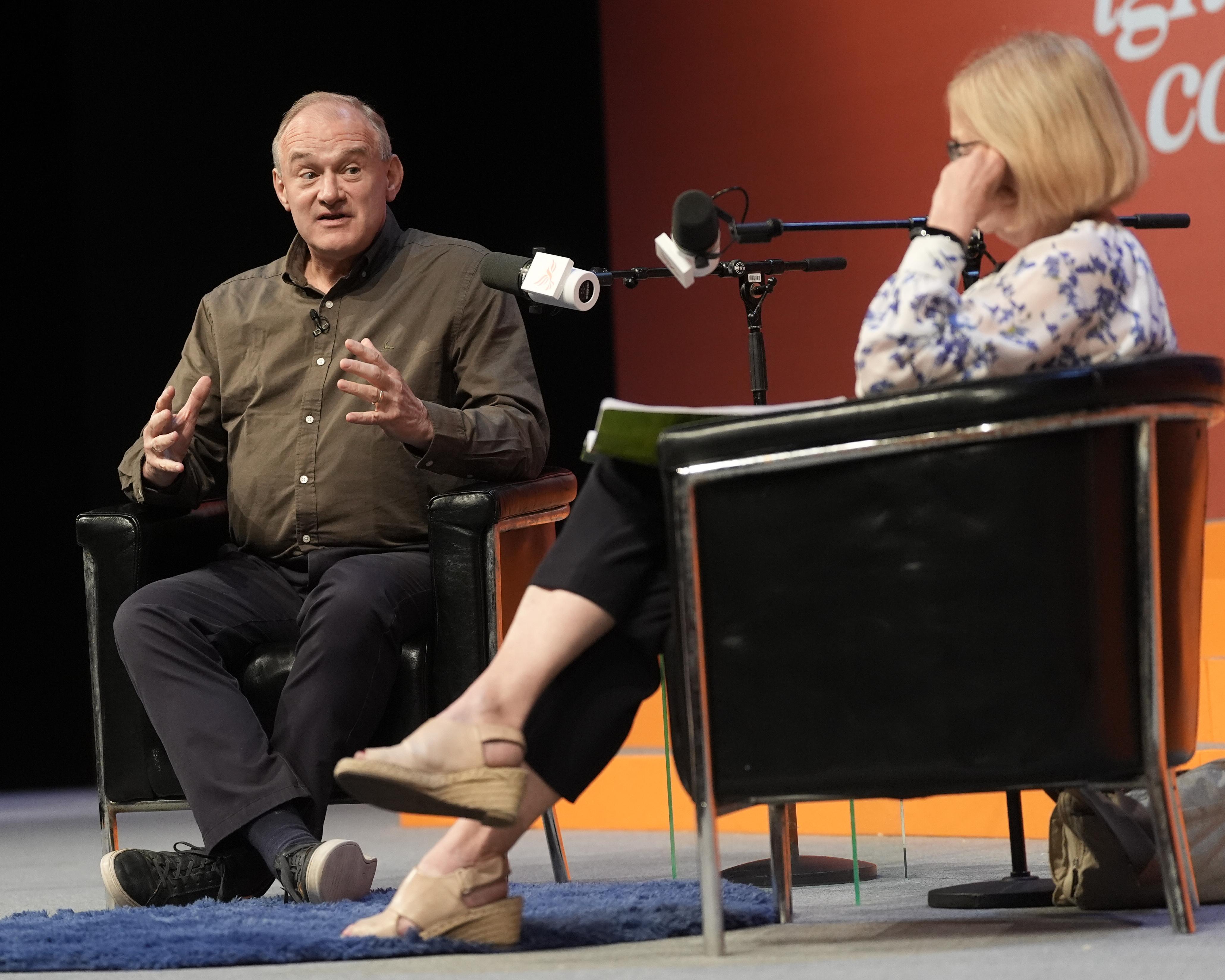 Two people sit in armchairs speaking into microphones during a staged discussion.