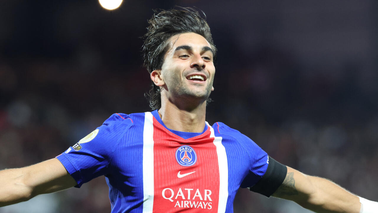 Smiling PSG footballer in blue and red jersey celebrates with arms outstretched under stadium lights