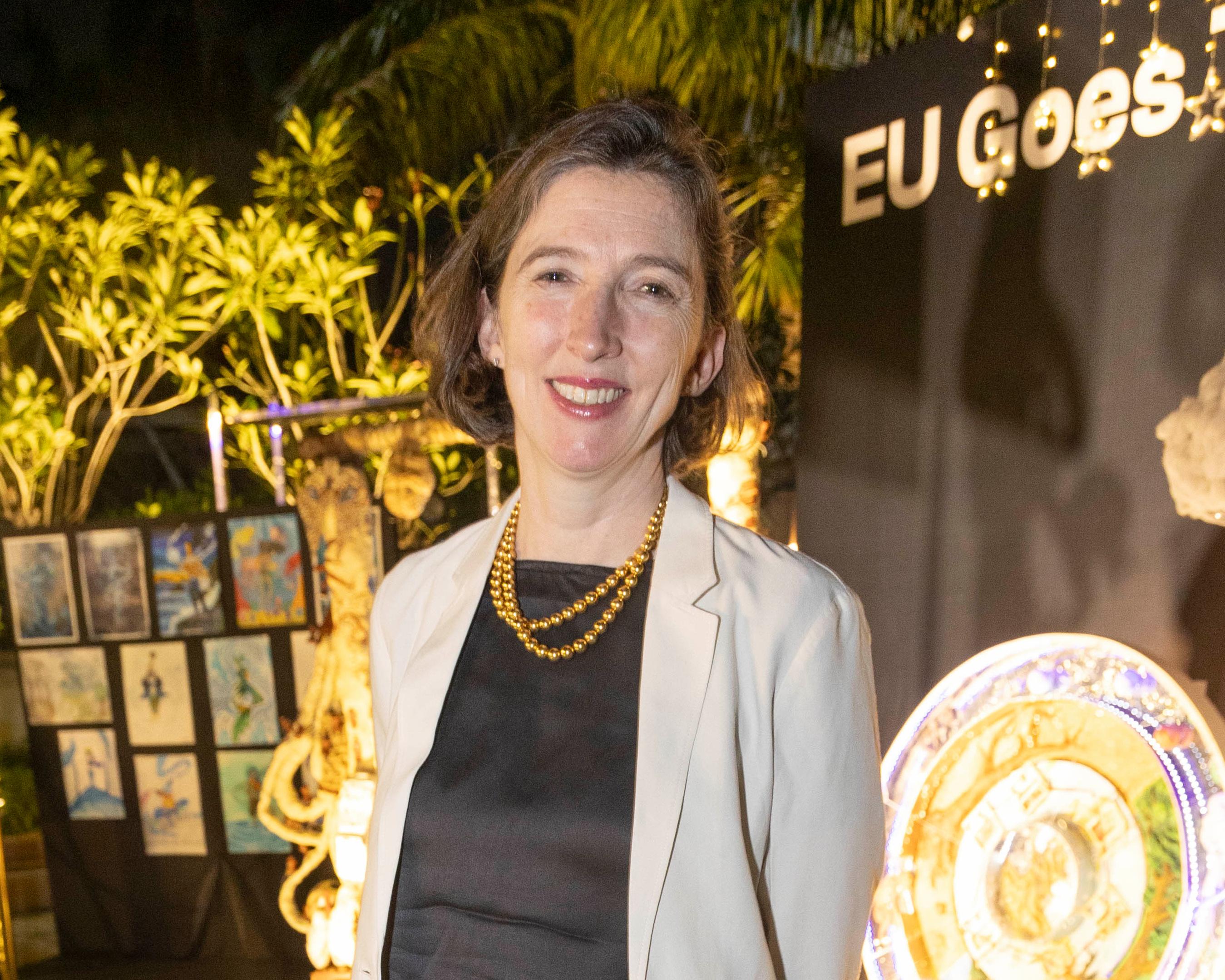 Smiling woman in white blazer and gold necklace at a warmly lit event