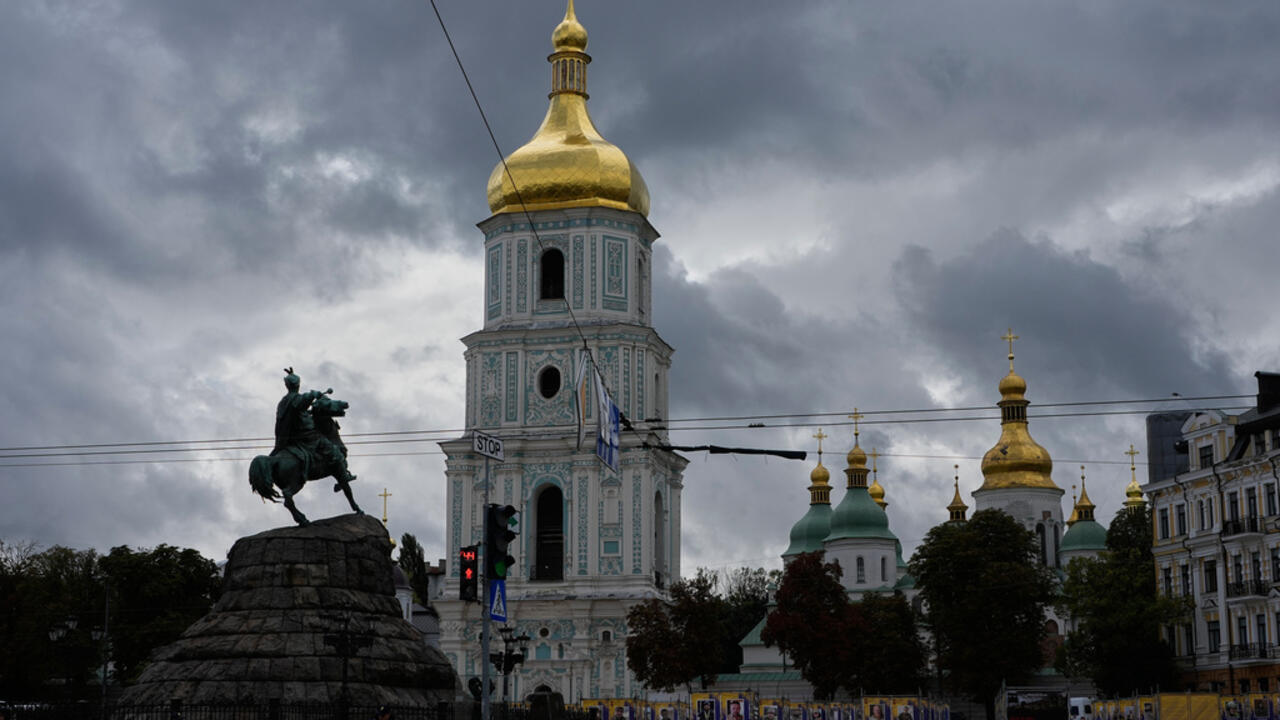 Kyiv cathedral domes and equestrian monument beneath dark storm clouds and overhead wires