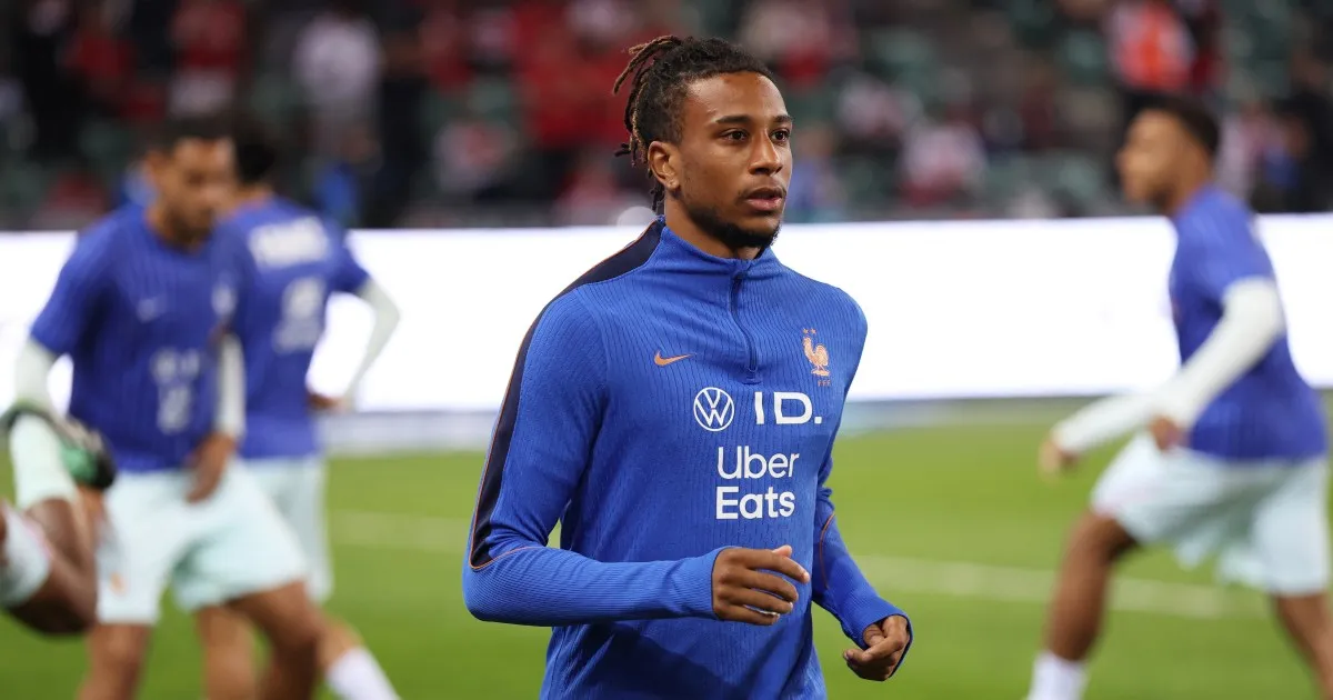 A France player in a blue training top jogs on the pitch as teammates warm up behind him.