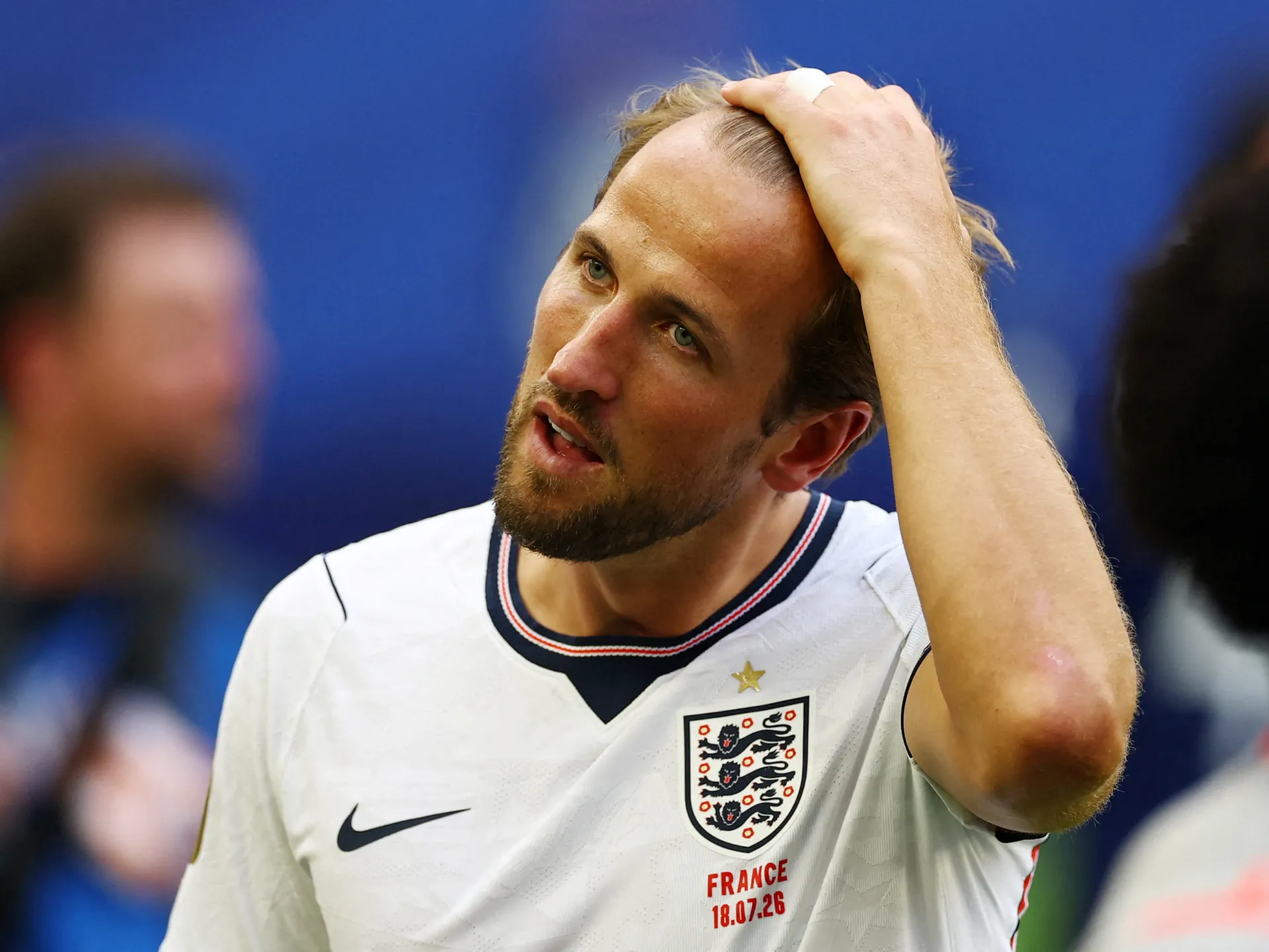 A footballer in an England shirt holds his head with one hand during a match.