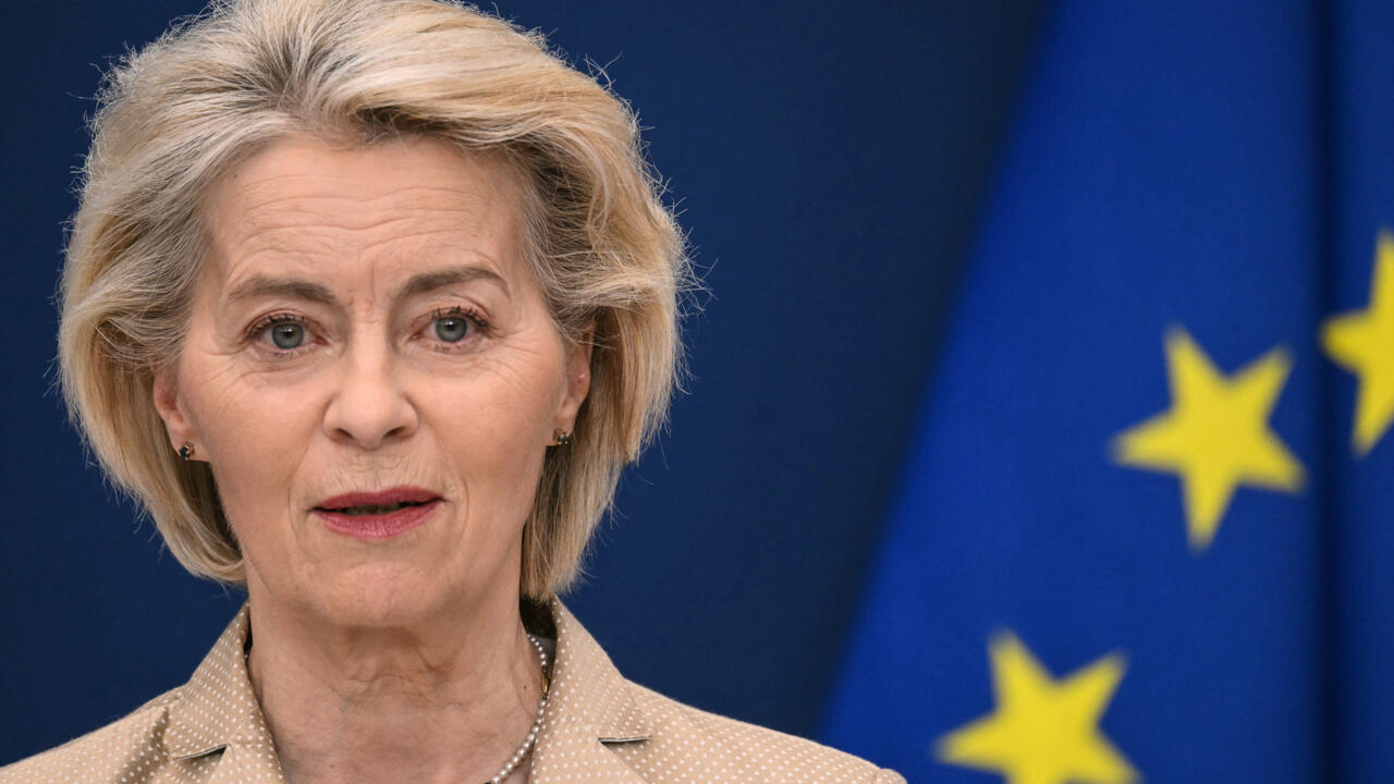 Close-up of a blonde woman speaking with European Union flags visible in the background