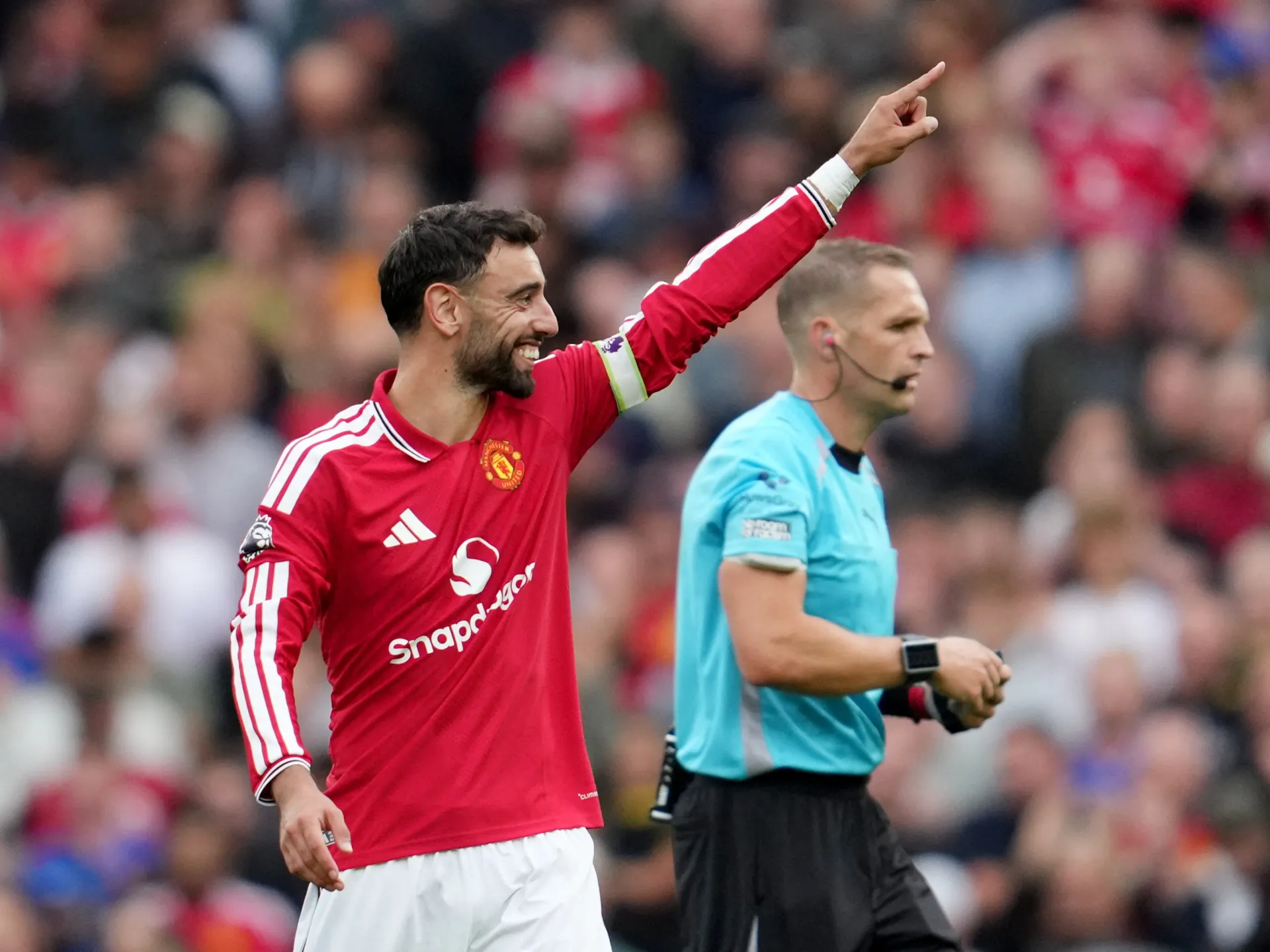 Manchester United player in red raises his arm beside a referee during a football match