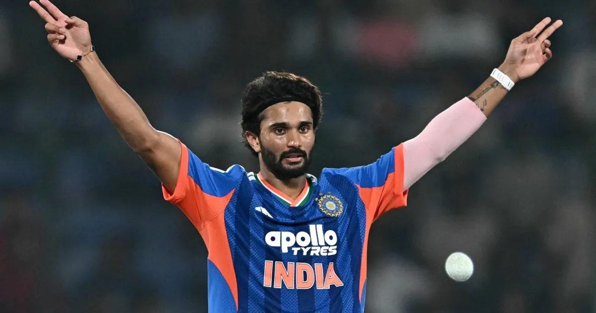 Indian cricket player raises both arms while wearing a blue and orange India jersey.
