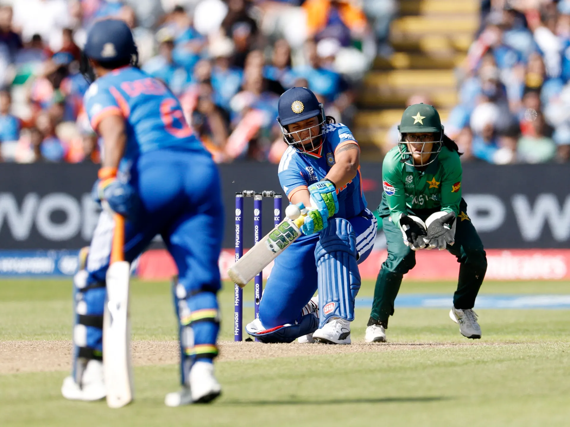 Indian batter plays a shot as Pakistan wicketkeeper crouches behind the stumps during a cricket match.