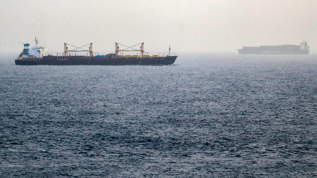 Two cargo ships travel across a hazy, choppy sea under an overcast sky.
