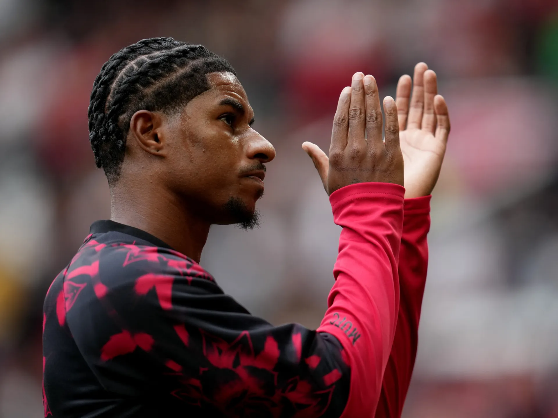 Football player in red and black raises both hands during a match