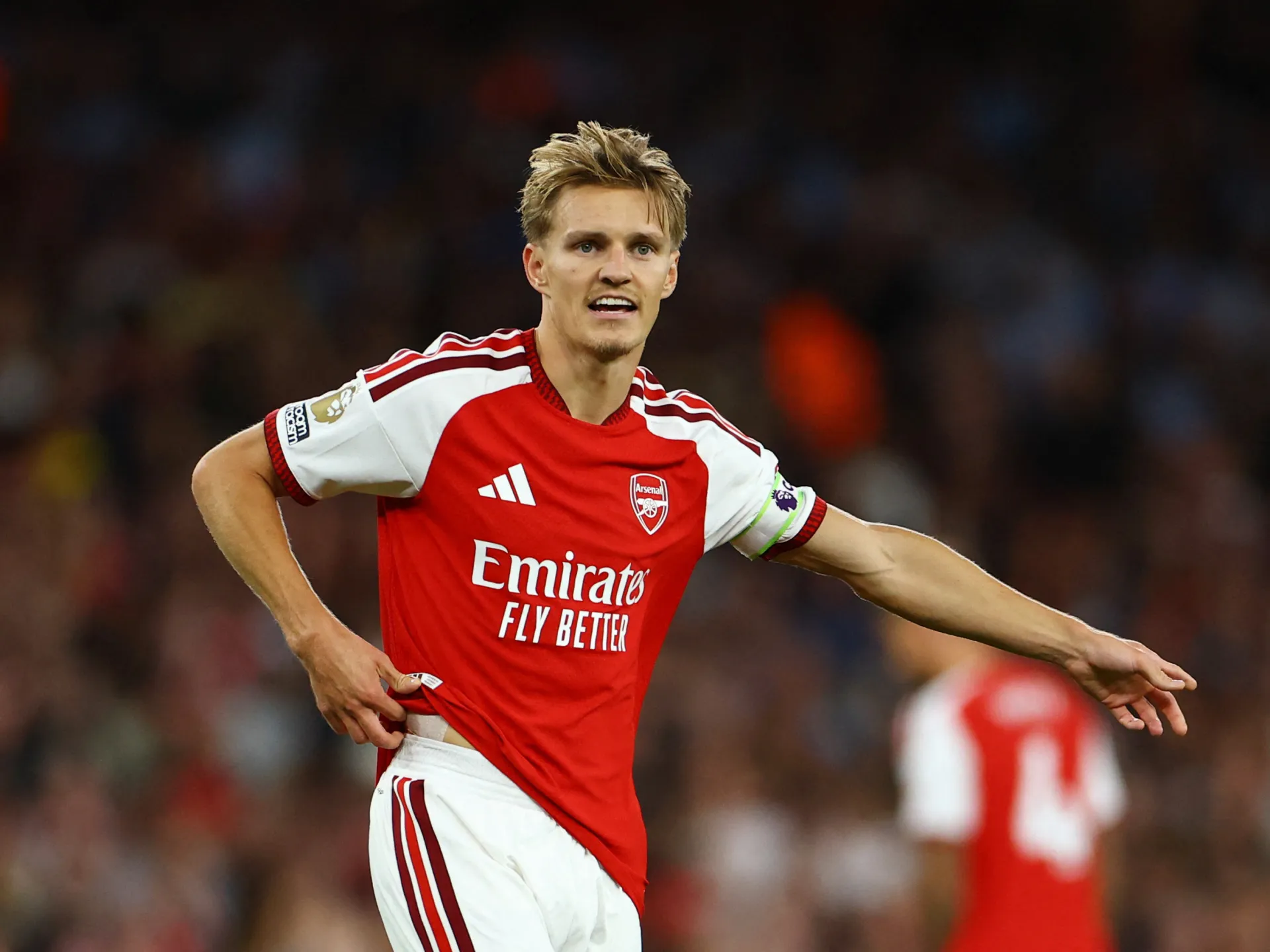 Arsenal player in red-and-white kit running with arms outstretched on the pitch