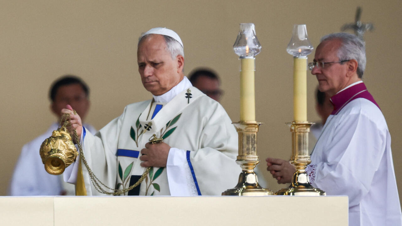 A priest holds a censer beside another clergyman and two tall lit candles.