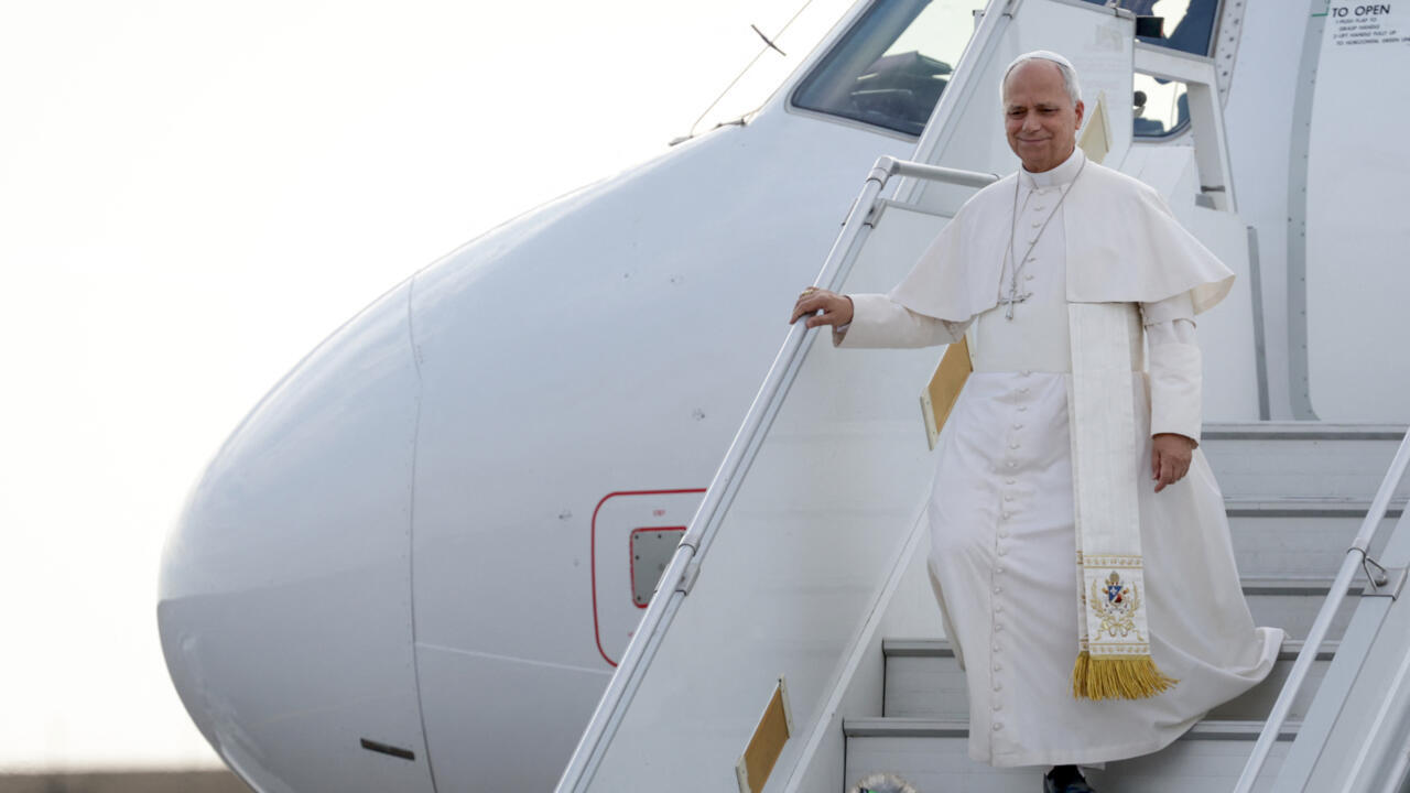 A man in white papal robes descends aircraft stairs beside the plane.