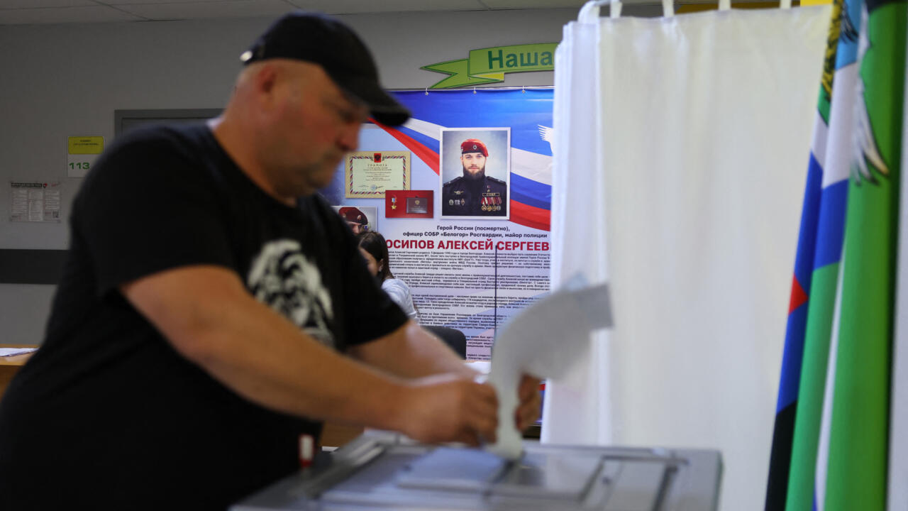 Man inserts a ballot into a transparent ballot box at a polling station.