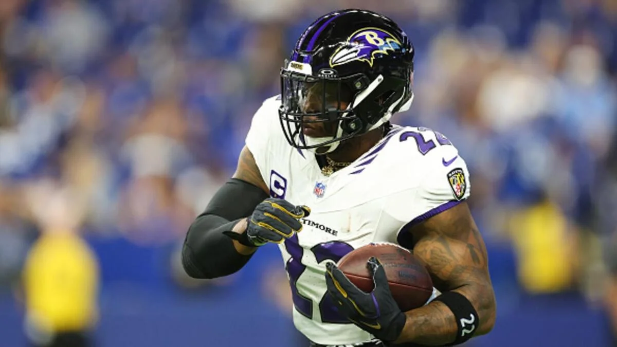 Ravens player in uniform carries a football while running during an NFL game