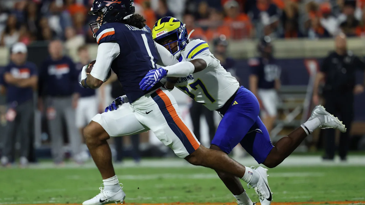A Delaware player in a white uniform tackles a navy-clad Virginia player carrying the football.