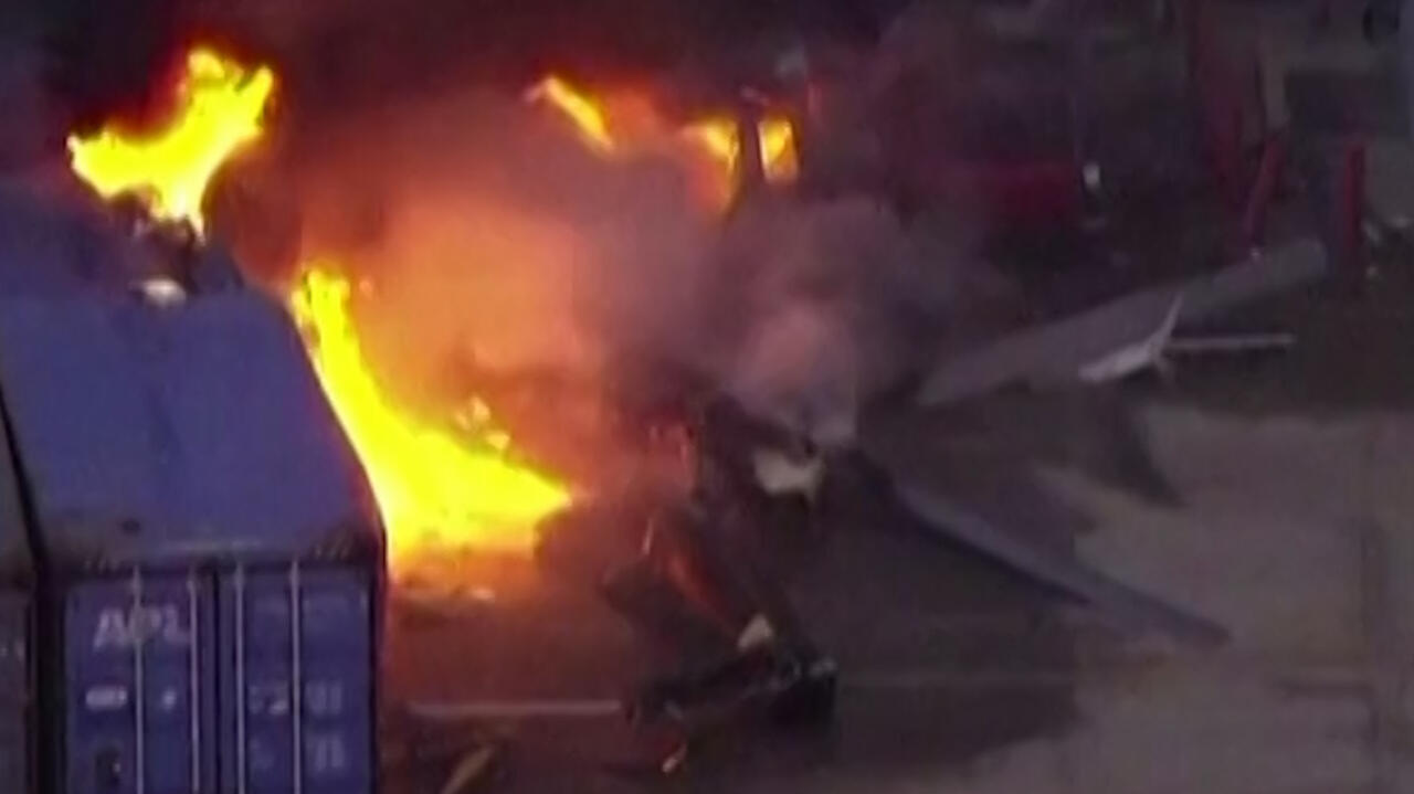 Burning helicopter wreckage amid smoke and debris at night