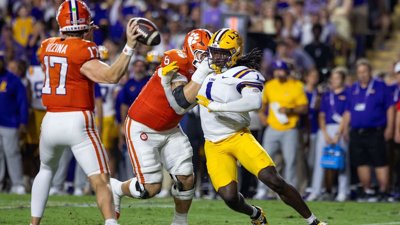 LSU football player runs with the ball as Clemson defenders pursue him on the field.