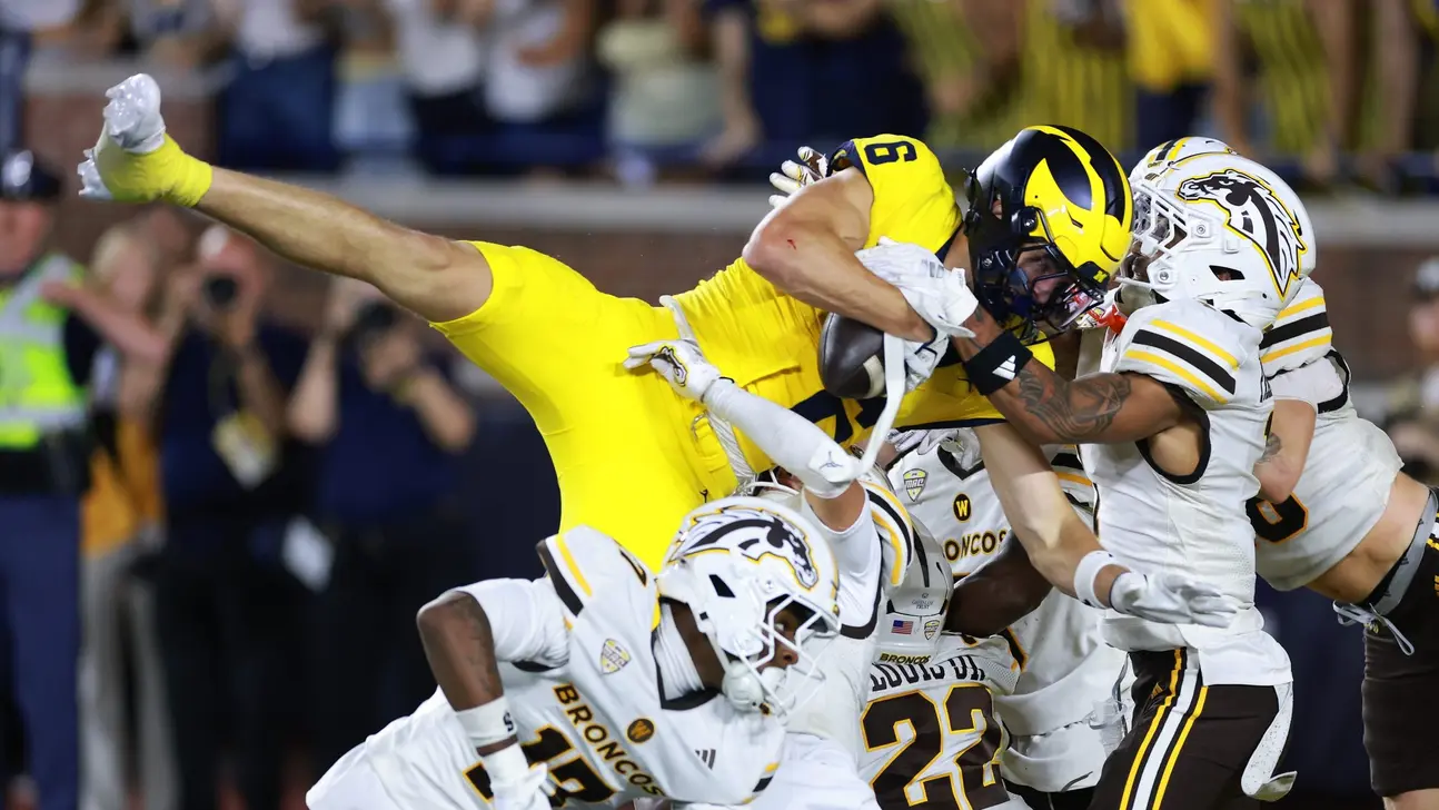 Michigan player reaches for the ball as Western Michigan defenders tackle him during a football game
