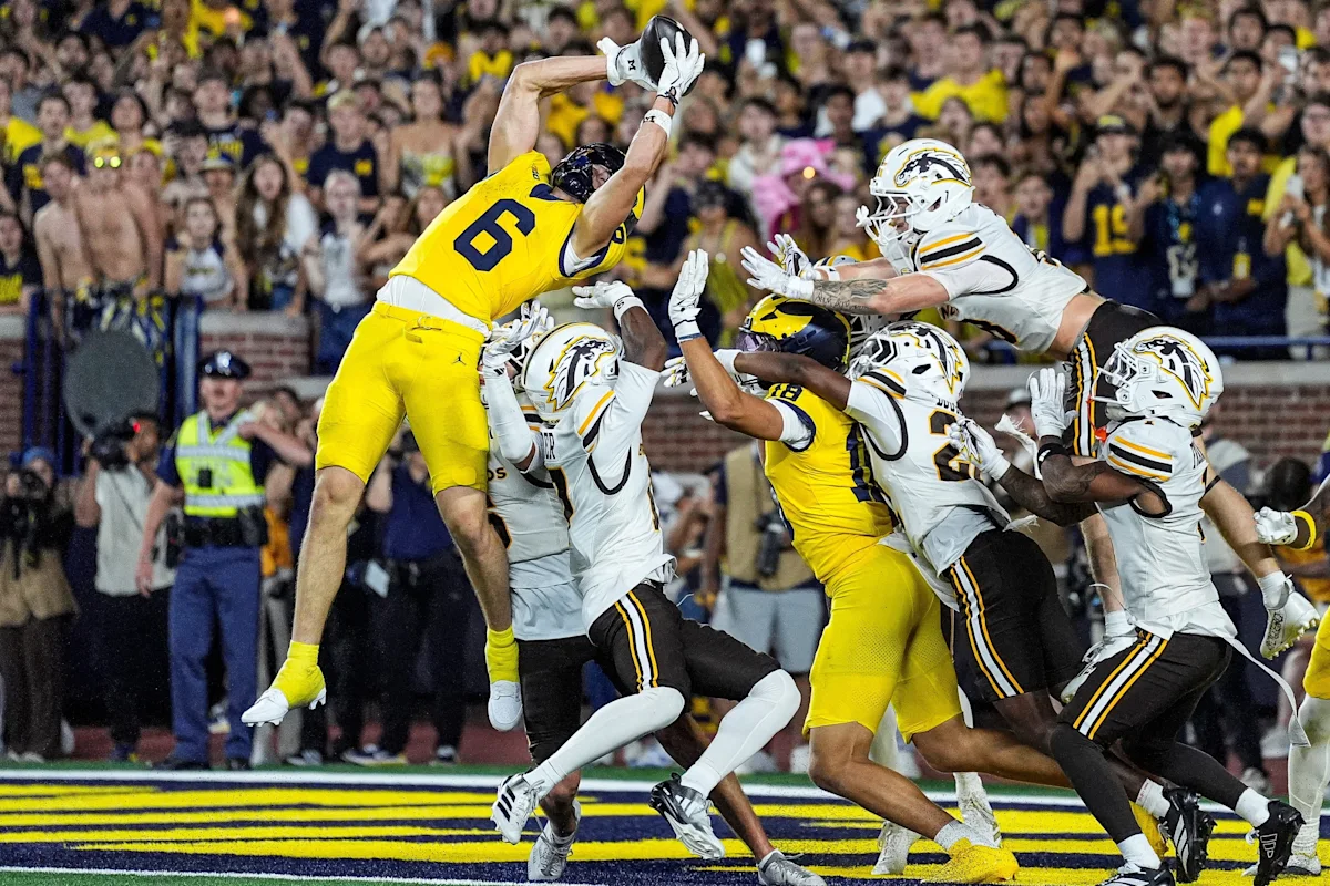 Michigan player leaps above defenders attempting to catch a football in the end zone