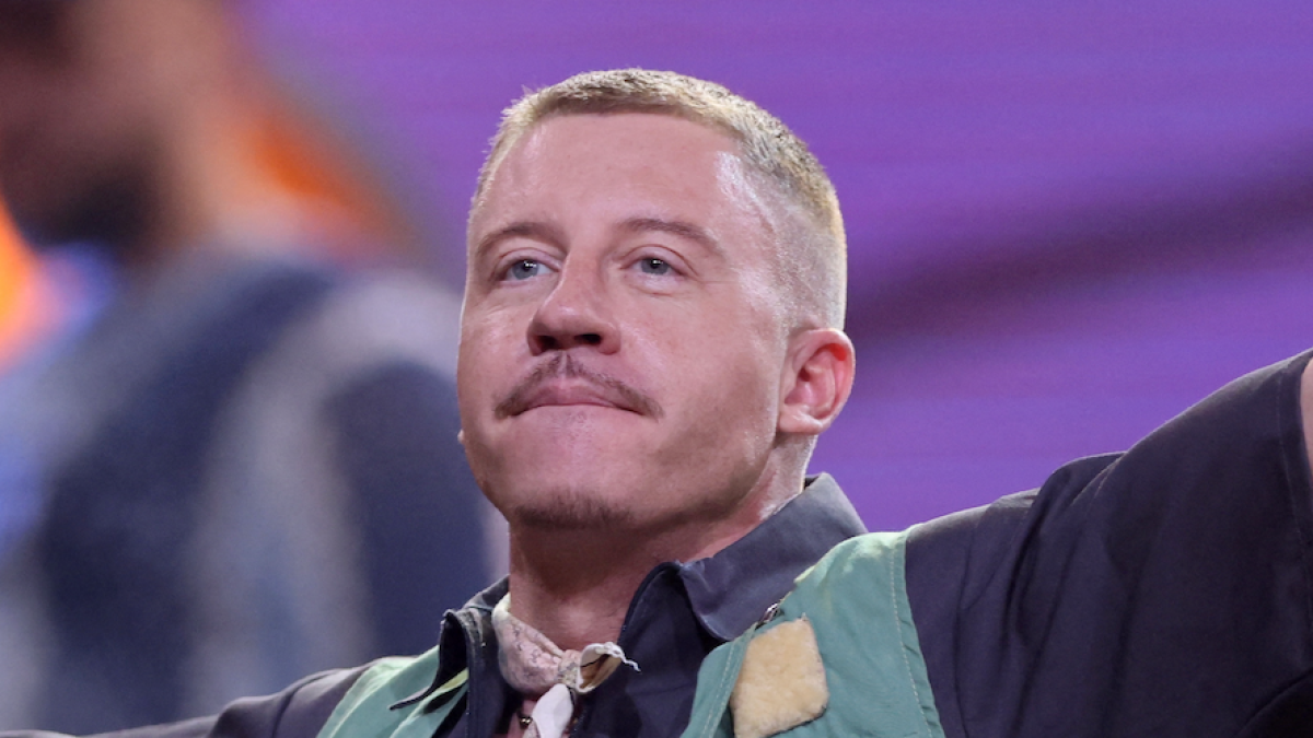Close-up of a short-haired man wearing a dark shirt and green vest under purple lighting