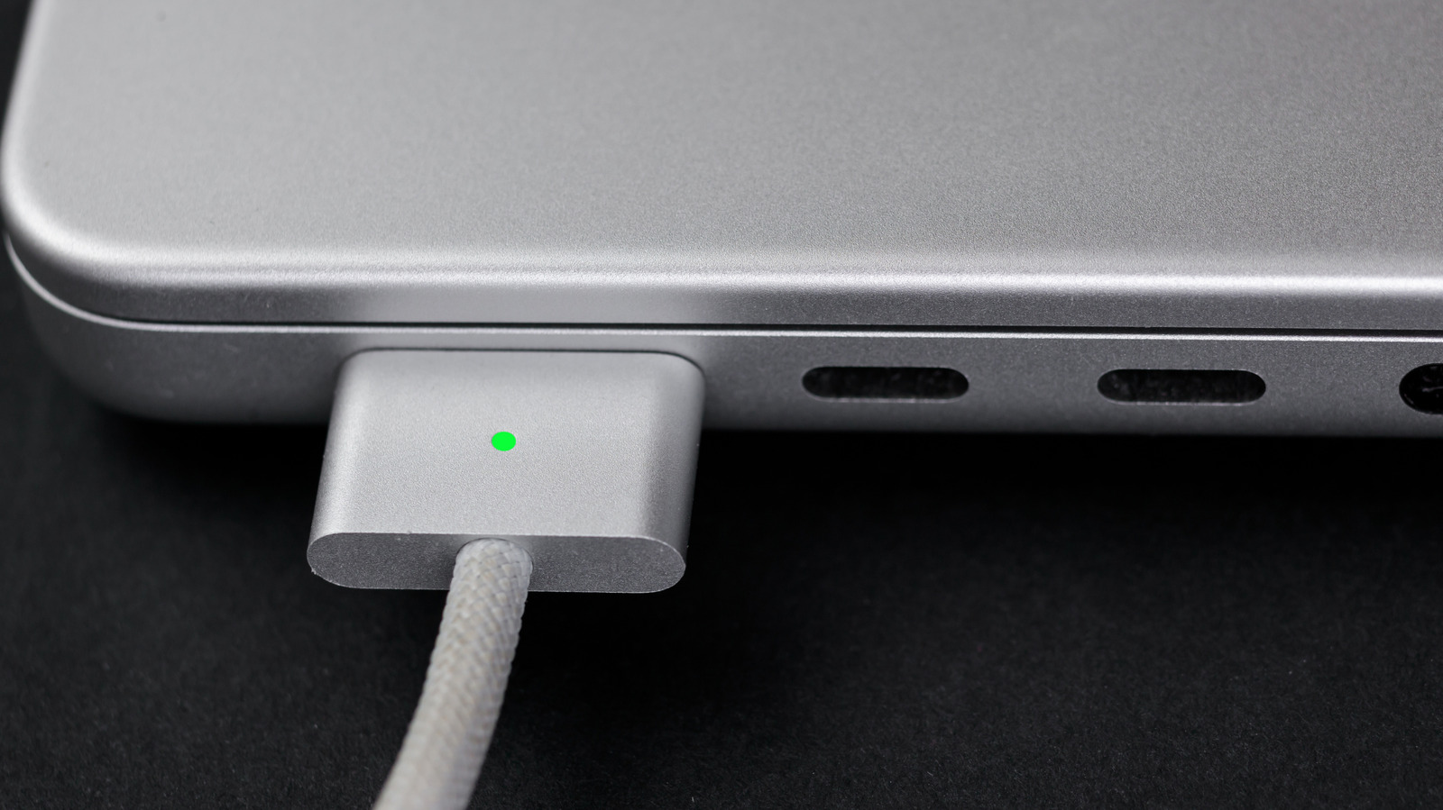 Close-up of a MacBook with a MagSafe charging connector attached and its green indicator illuminated.