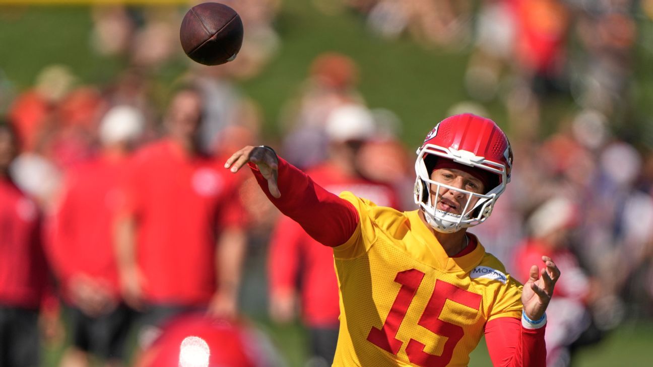 Quarterback in a red helmet and yellow jersey throws a football during practice.
