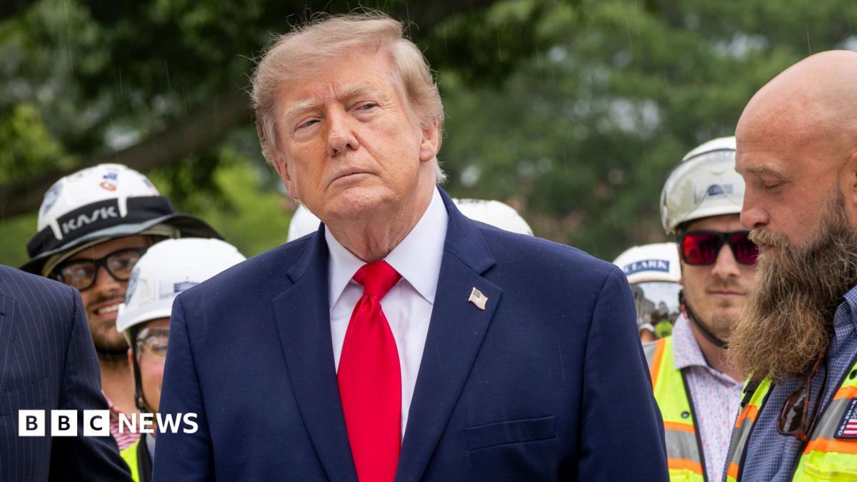 Donald Trump stands in a suit among construction workers outdoors, with BBC News branding visible.