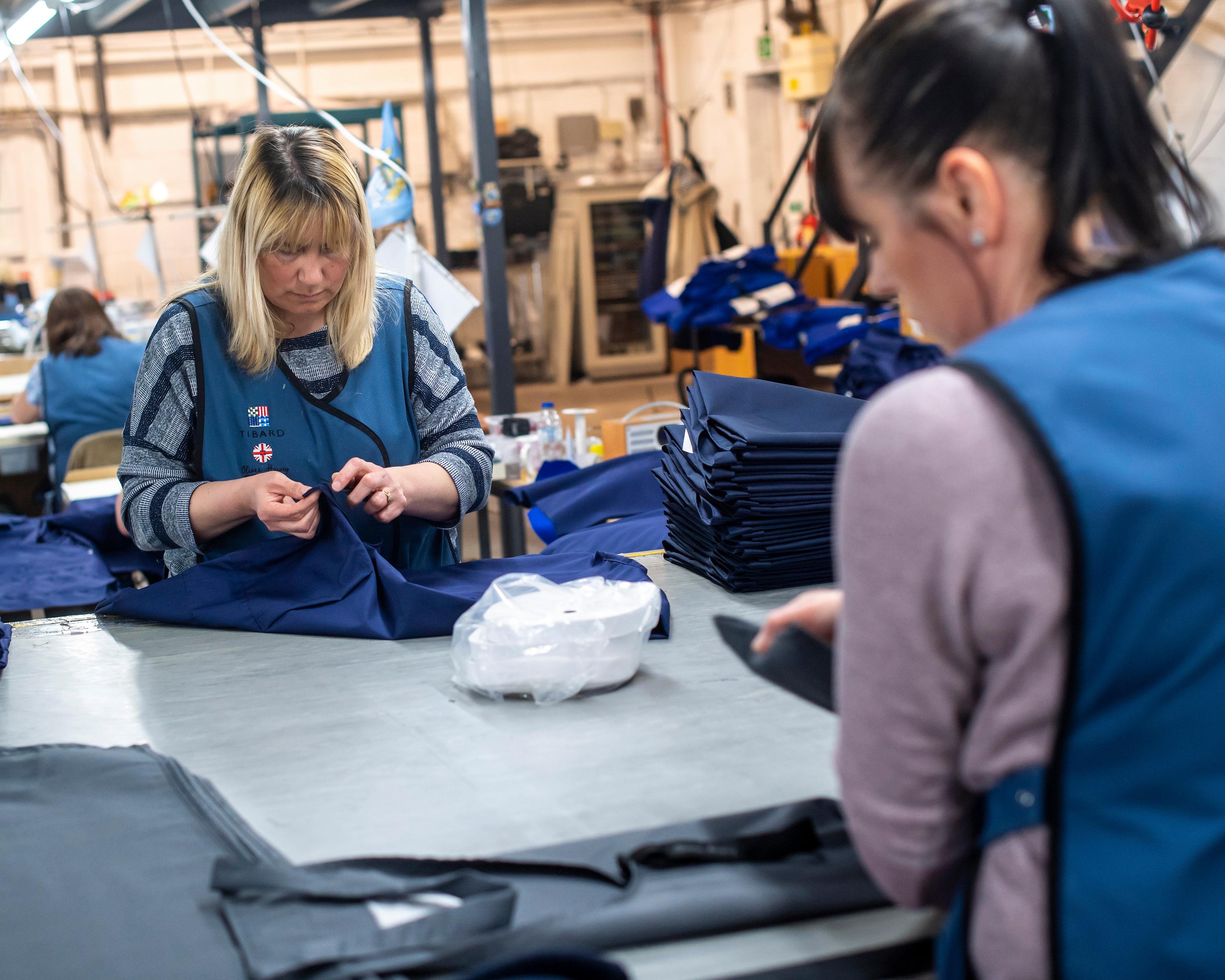 Workers sew and fold navy blue garments at a busy industrial clothing production table.