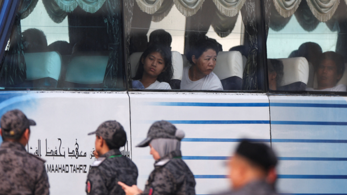 Passengers sit inside a bus as uniformed officers stand outside beside its windows.