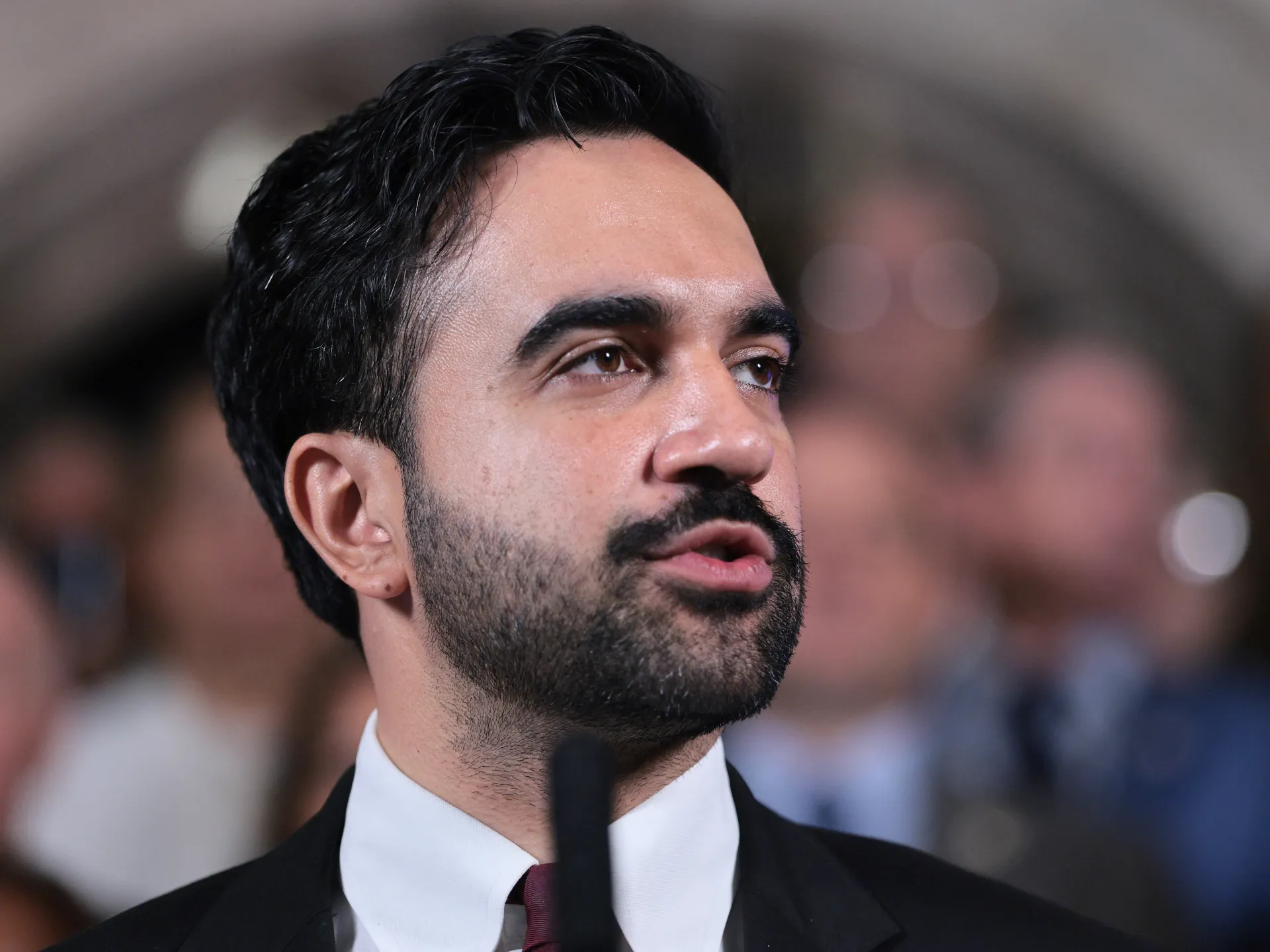 Bearded man in a suit speaking with a blurred audience behind him