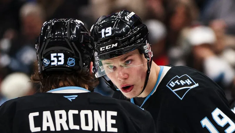 Two hockey players in black helmets and jerseys face each other during a game