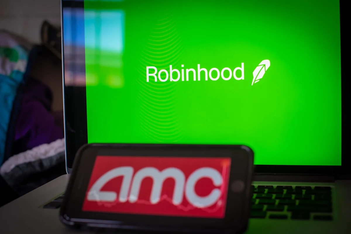 Laptop displaying Robinhood logo behind smartphone showing AMC logo